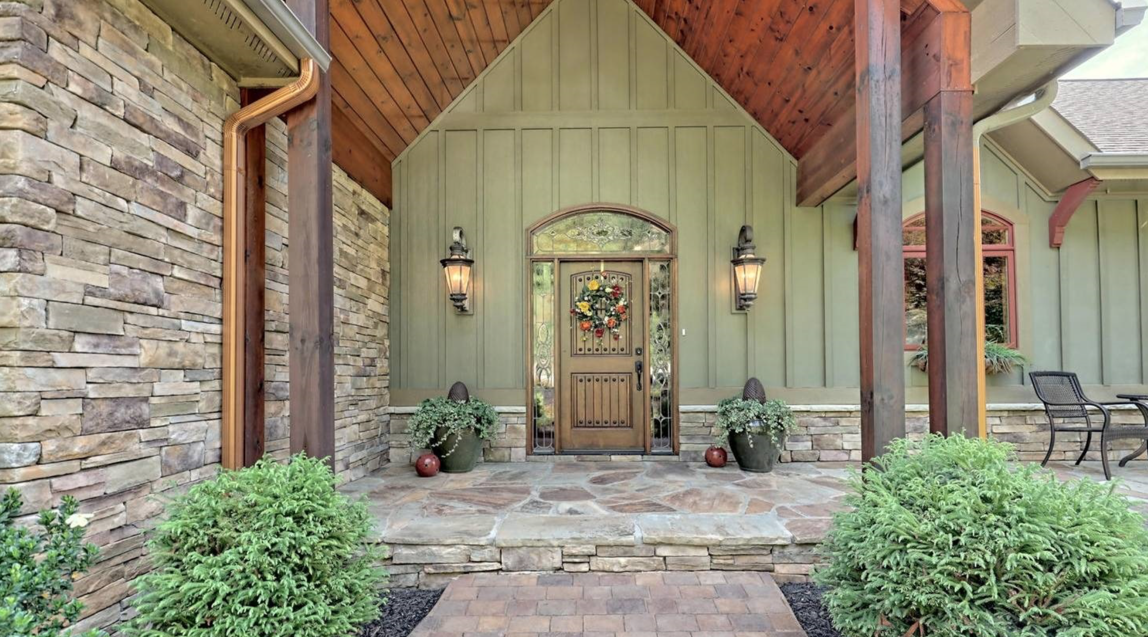 Beautiful Front exterior of Lakefront home in Young Harris Georgia. It is sage green with stone walls and wood plank lined overhang in Cherry stain.