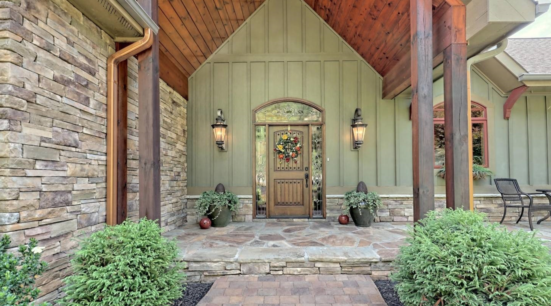 North Georgia Mountains Homes Beautiful Front exterior of Lakefront home in Young Harris Georgia. It is sage green with stone walls and wood plank lined overhang in Cherry stain.